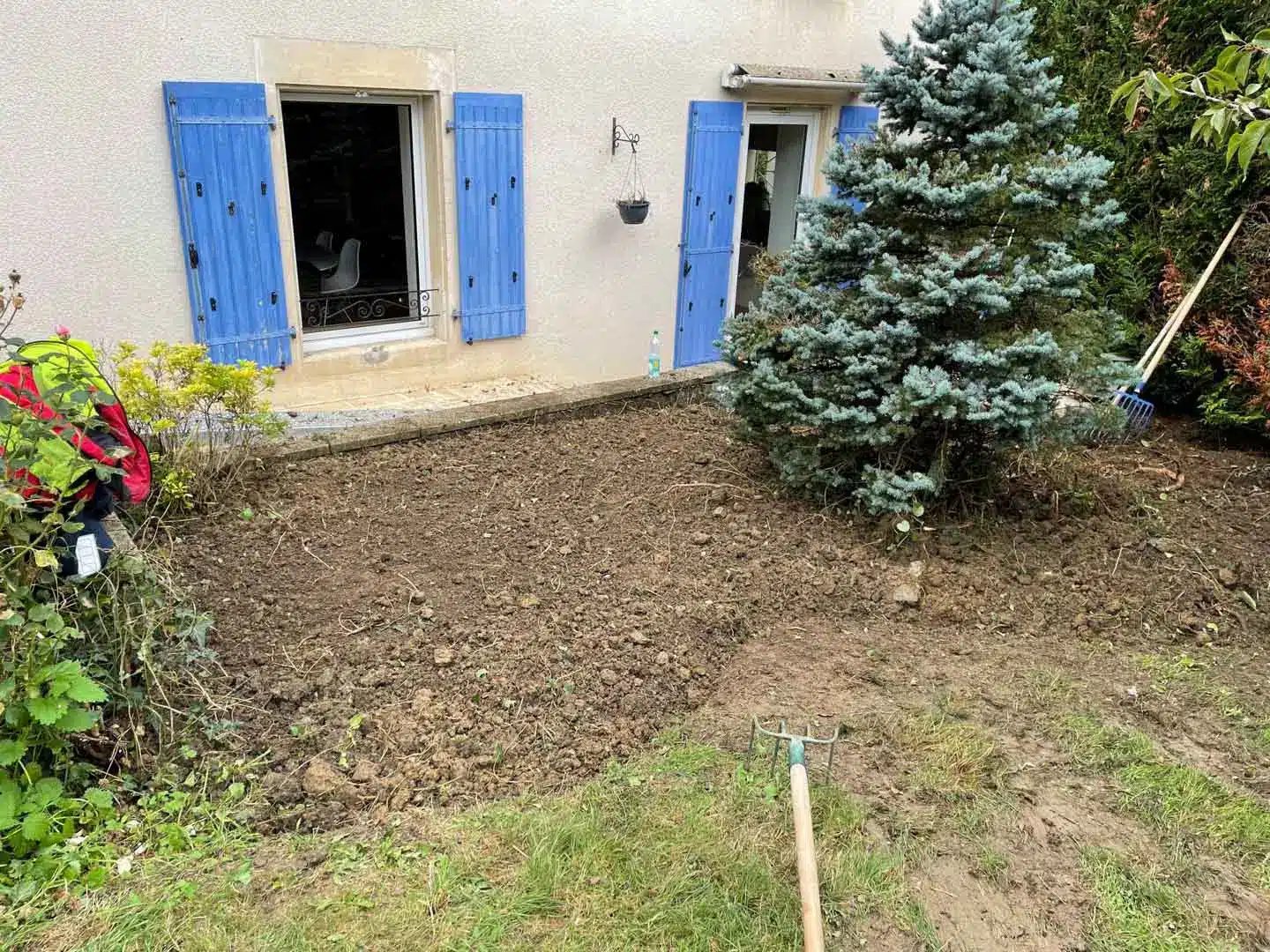 Terre travaillée devant une maison aux volets bleus